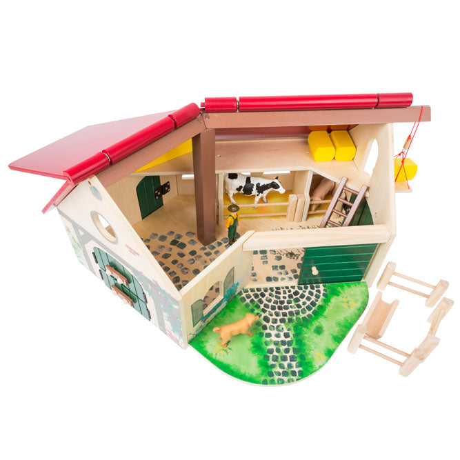 La construcción de madera de la granja juguete está dispuesta en forma de ángulo  y equipada con un techo plegable. Detalle con el techo abierto.